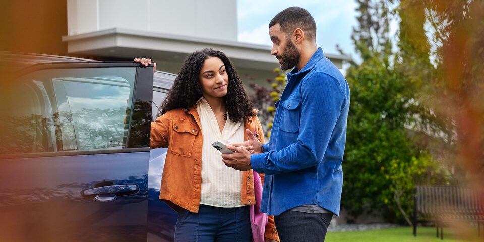 Pareja usando tecnología de conectividad Chevrolet junto a su auto para mayor seguridad y comodidad