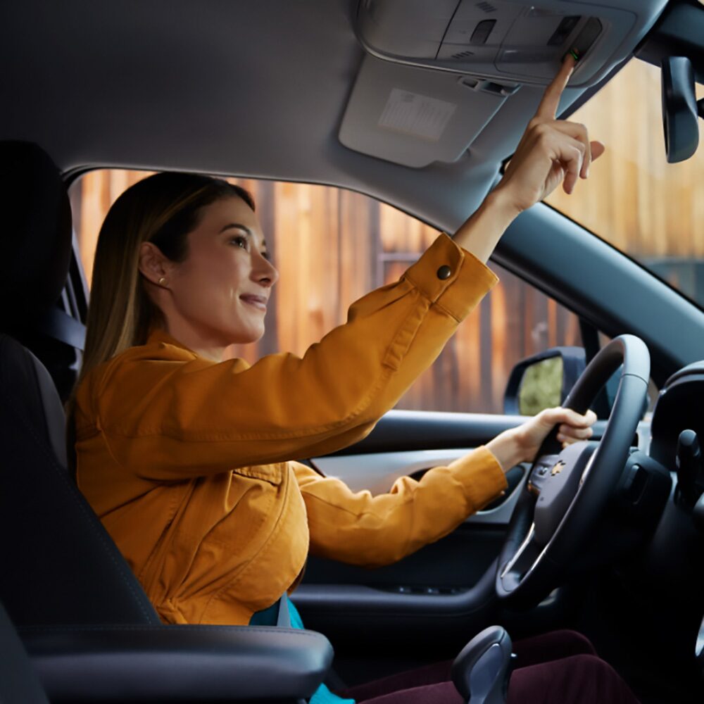 Imagen de una mujer sentada en el asiento de conductor de un vehículo Chevrolet mientras presiona el botón de OnStar en frente del espejo retrovisor.