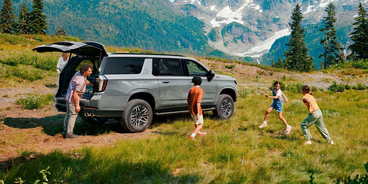 Imagen que muestra a tres niños jugando al lado de una Chevrolet Suburban Z71 estacionada en la montaña, mientras su padre los observa y saca cosas del baúl.