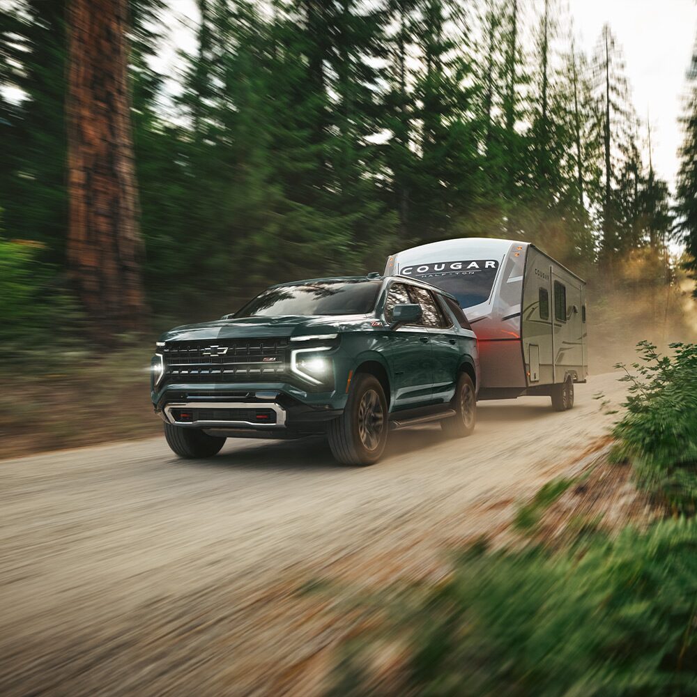 Chevrolet Suburban Z71 remocalndo un trailer por un camino de tierra en un bosque.
